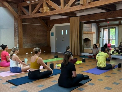 People seated on yoga mats in a museum room with exposed wooden beams.
