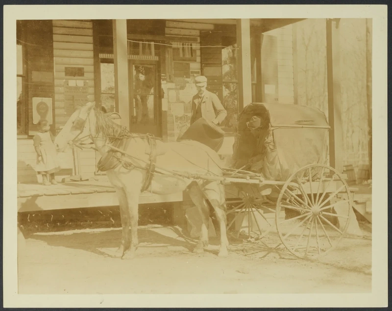 A horse-drawn covered wagon beside a wooden building with a man and two children
