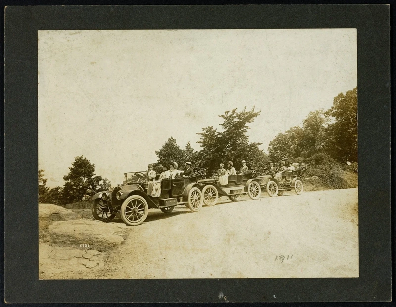 People riding in historic automobiles on a country road